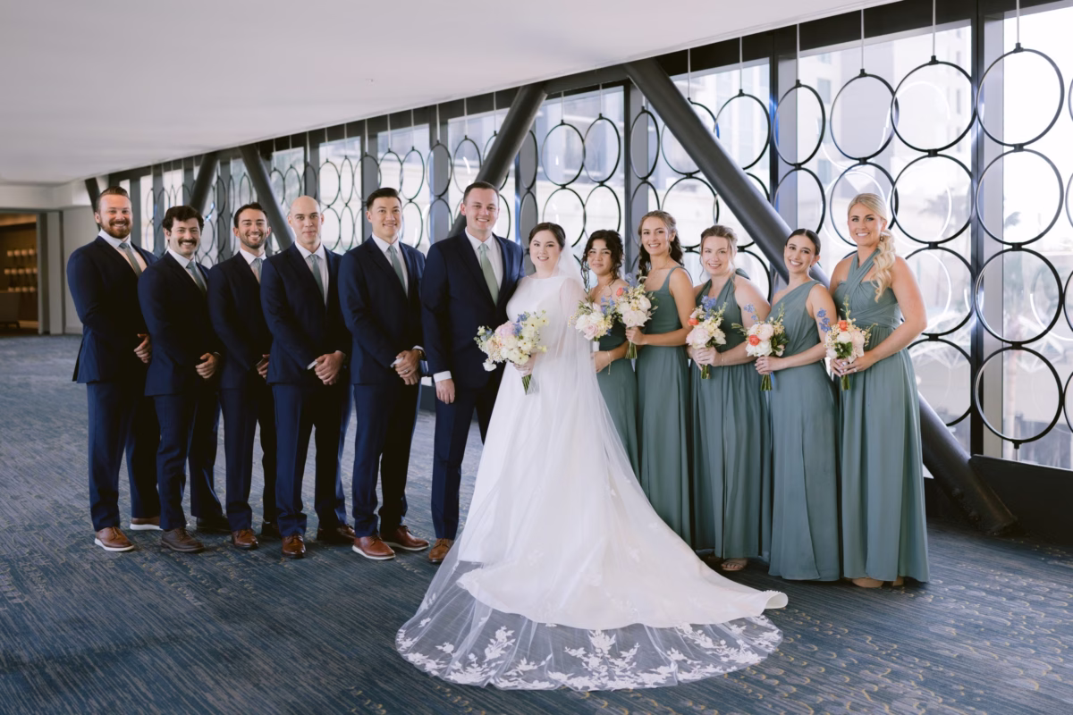 Wedding party portrait with sage green bridesmaids and navy groomsmen at Armature Works Tampa with floral arrangements by I Dew Events