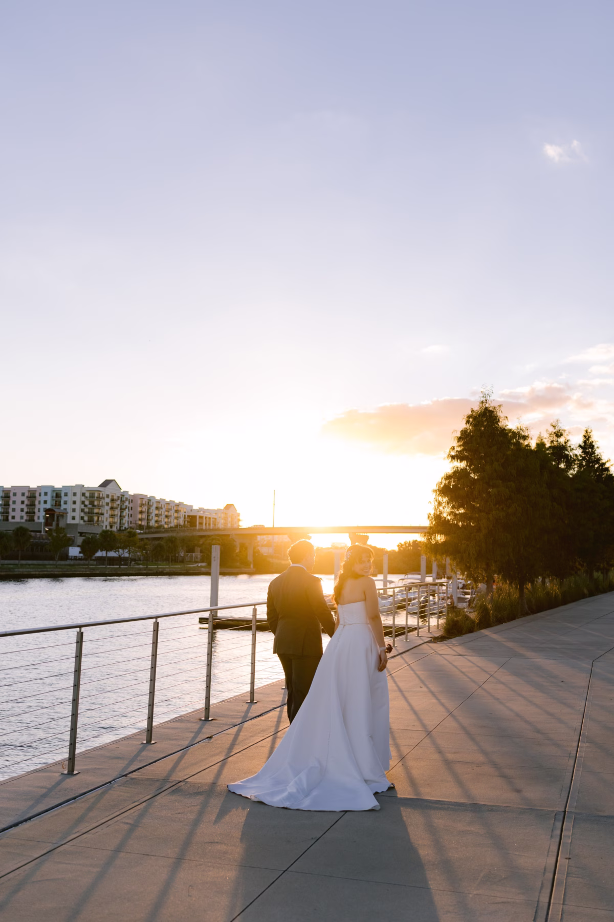 Bride and groom walking along waterfront boardwalk at sunset during their Armature Works wedding in Tampa planned by Seashine Weddings