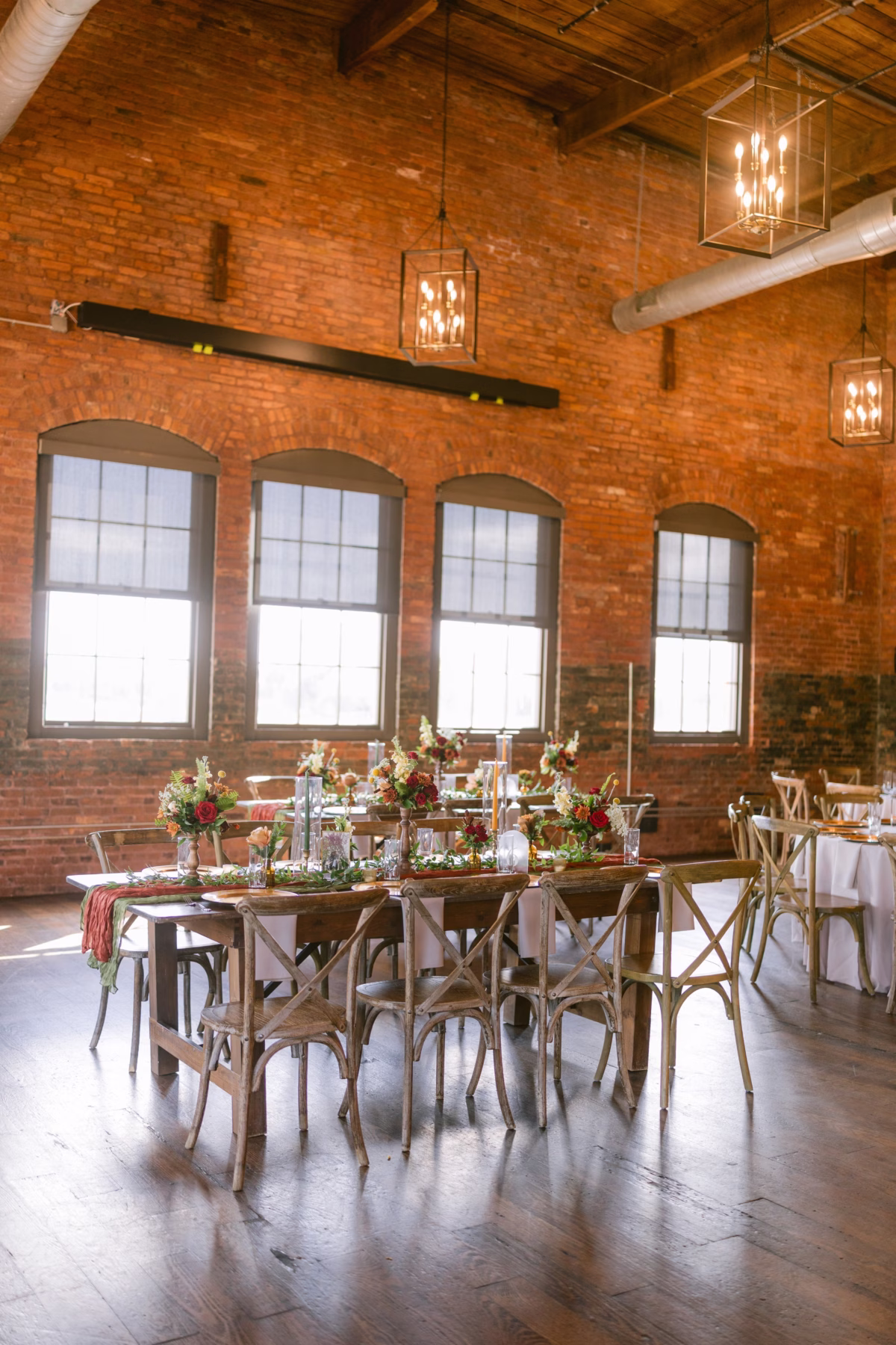 Elegant wedding reception tablescape with burgundy florals by Events in Bloom at Armature Works industrial venue in Tampa featuring exposed brick walls and lantern lighting