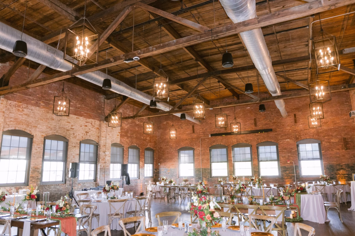 Industrial wedding reception space at Armature Works in Tampa featuring exposed brick walls, wooden ceiling beams, and elegant table settings