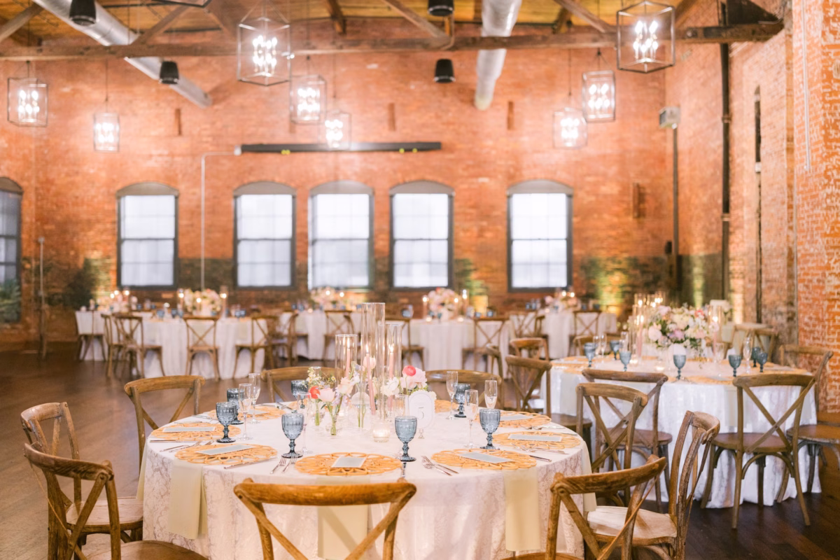 Elegant wedding reception at Armature Works Tampa with exposed brick walls, rustic wooden tables, and floral centerpieces by I Dew Events and Logan Paradiso planning