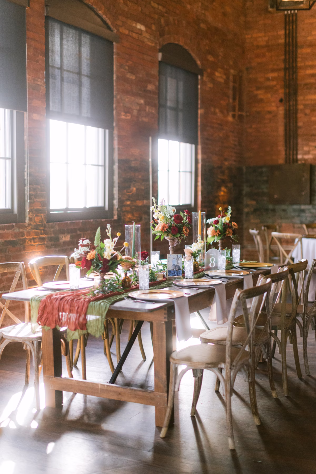 Rustic wedding reception tablescape with colorful floral centerpieces by Events in Bloom at Armature Works Tampa featuring exposed brick walls and natural lighting