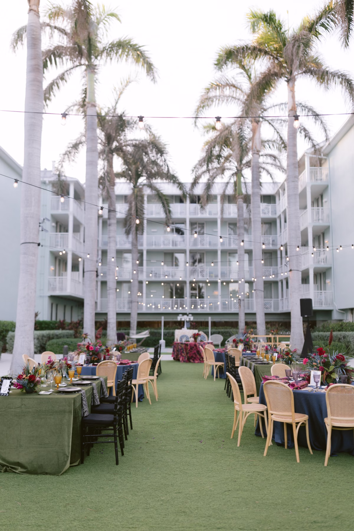 Outdoor wedding reception with jewel tone florals by Arms of Persephone at Casa Marina Key West featuring string lights and tropical palm trees
