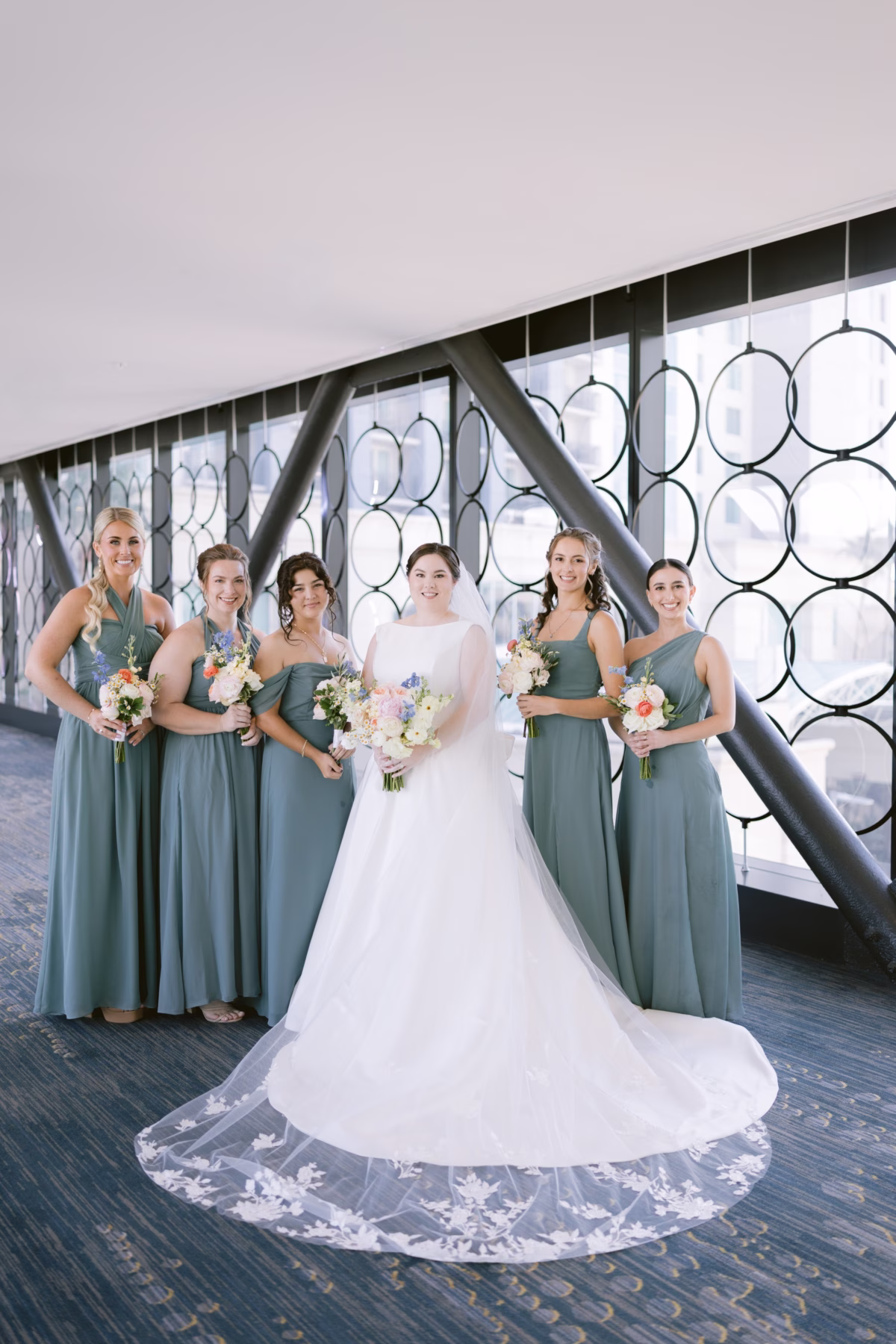 Bride in white dress from The White Closet Bridal with bridesmaids wearing sage green Birdy Grey dresses holding bouquets by I Dew Events at Armature Works Tampa wedding