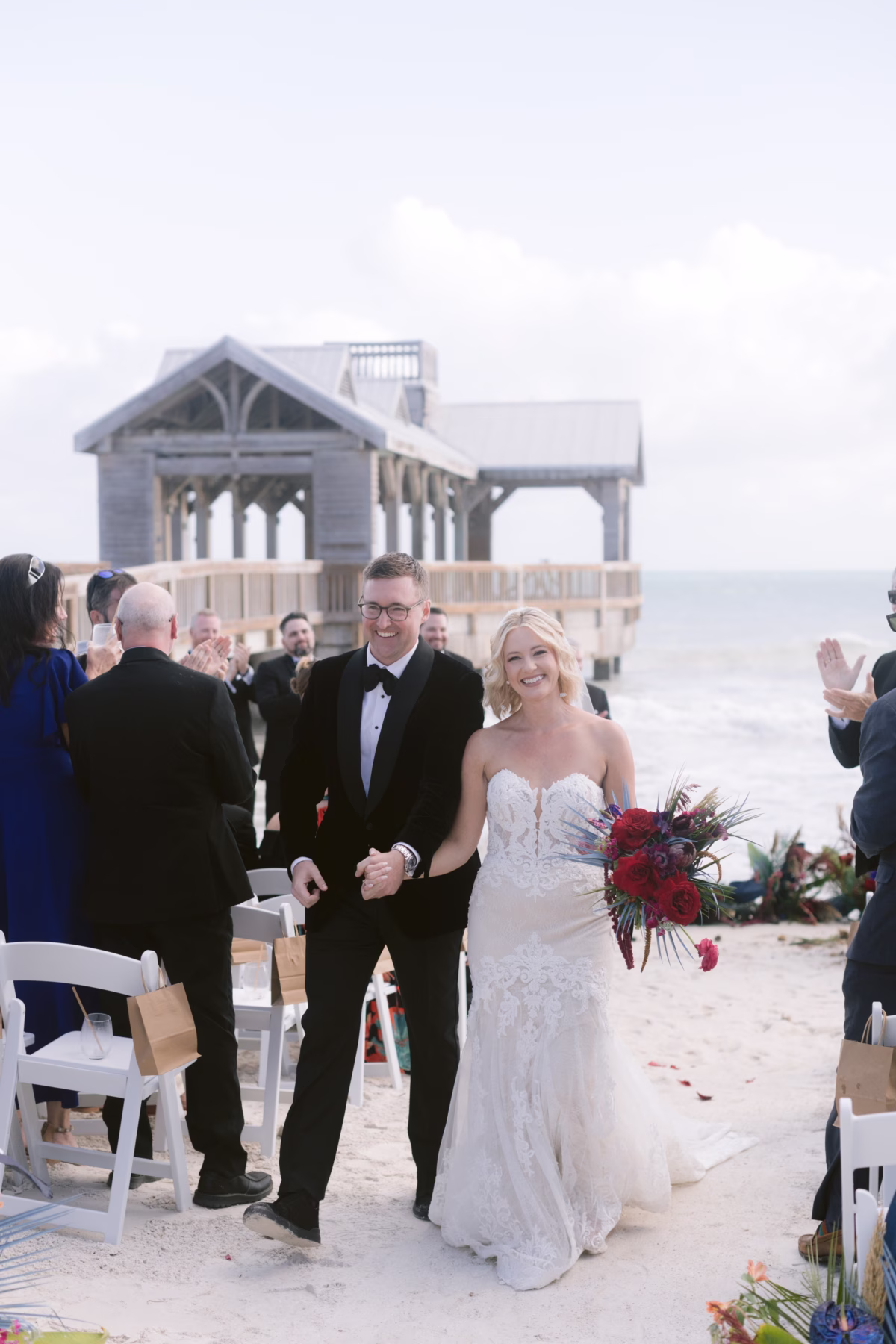 Newlyweds walk down the aisle after their beach wedding ceremony at Casa Marina Key West with red bouquet by Arms of Persephone