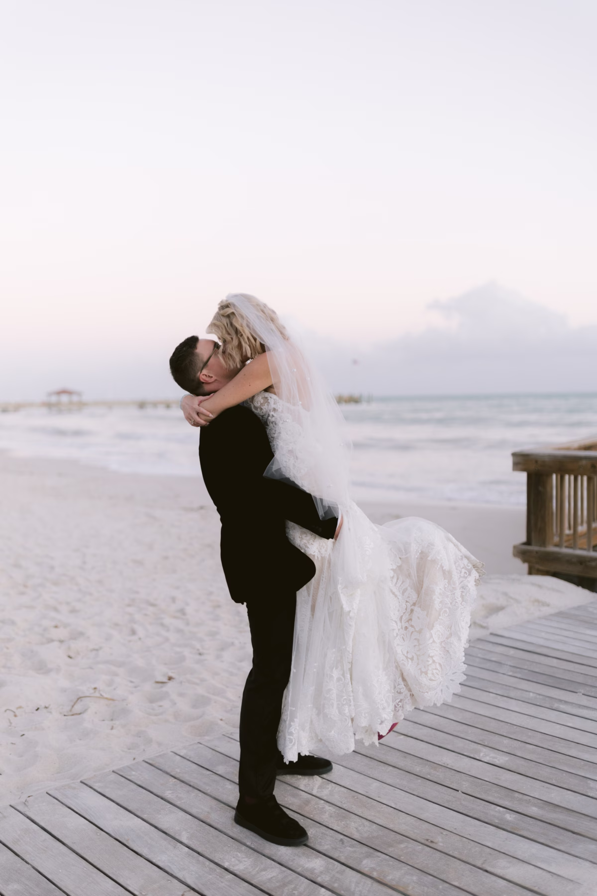 Groom lifting bride on wooden boardwalk at Casa Marina Key West beach wedding photographed by Ashley Izquierdo Photography