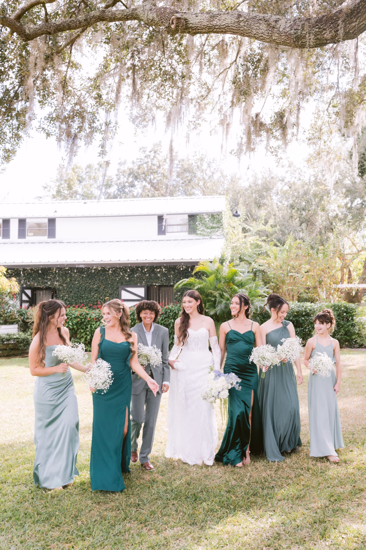 Bride in white gown with bridesmaids in emerald and sage green dresses holding white baby's breath bouquets by Ava Elise Decor at Soire Estate Tampa wedding photographed by Ashley Izquierdo Photography