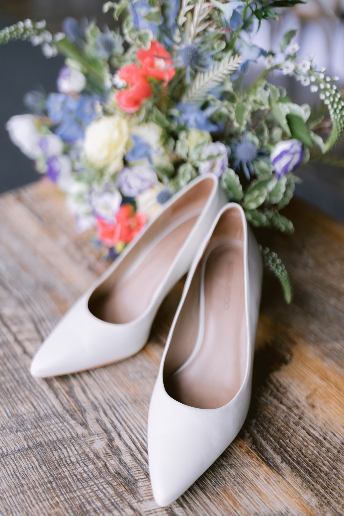 White bridal heels positioned next to wildflower wedding bouquet by Cherry Brandy Designs at Red Maple Vineyard wedding