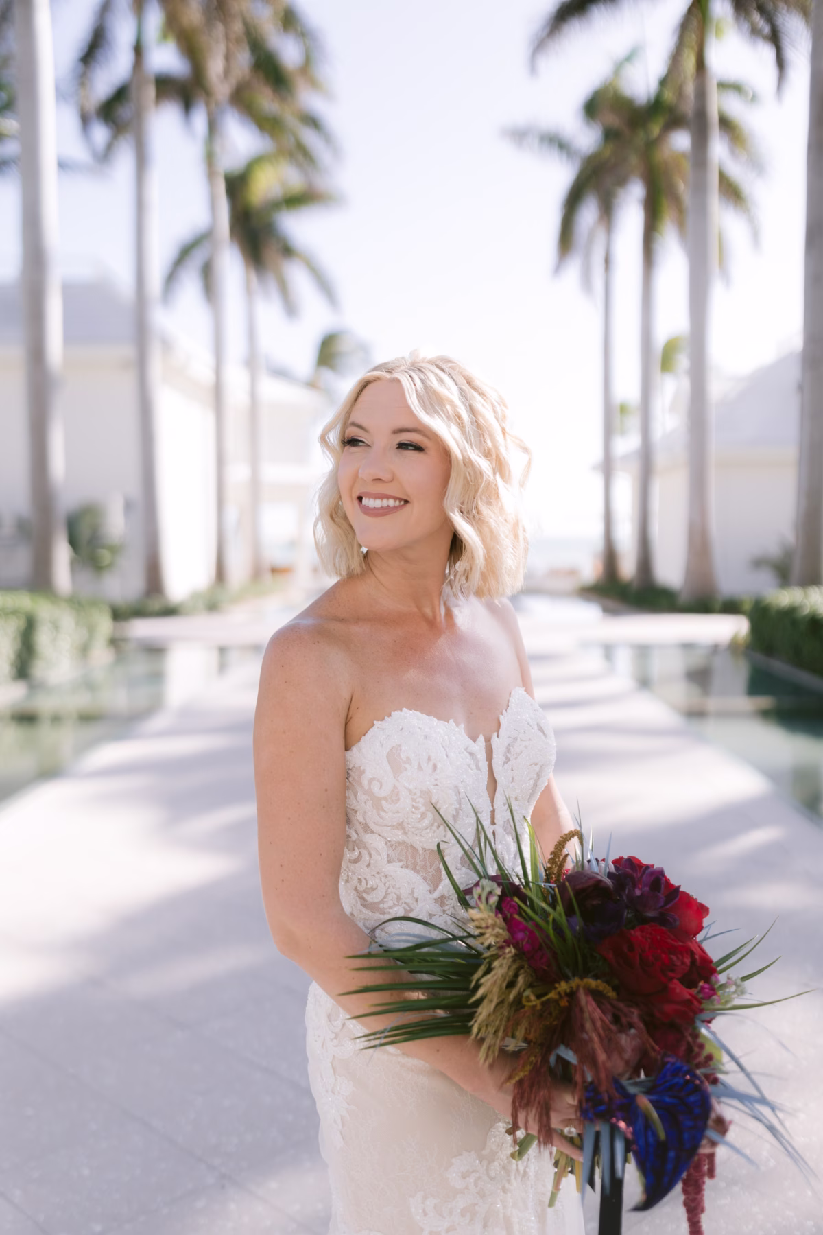 Bride holding jewel tone bouquet by Arms of Persephone at Casa Marina Key West wedding venue with palm trees