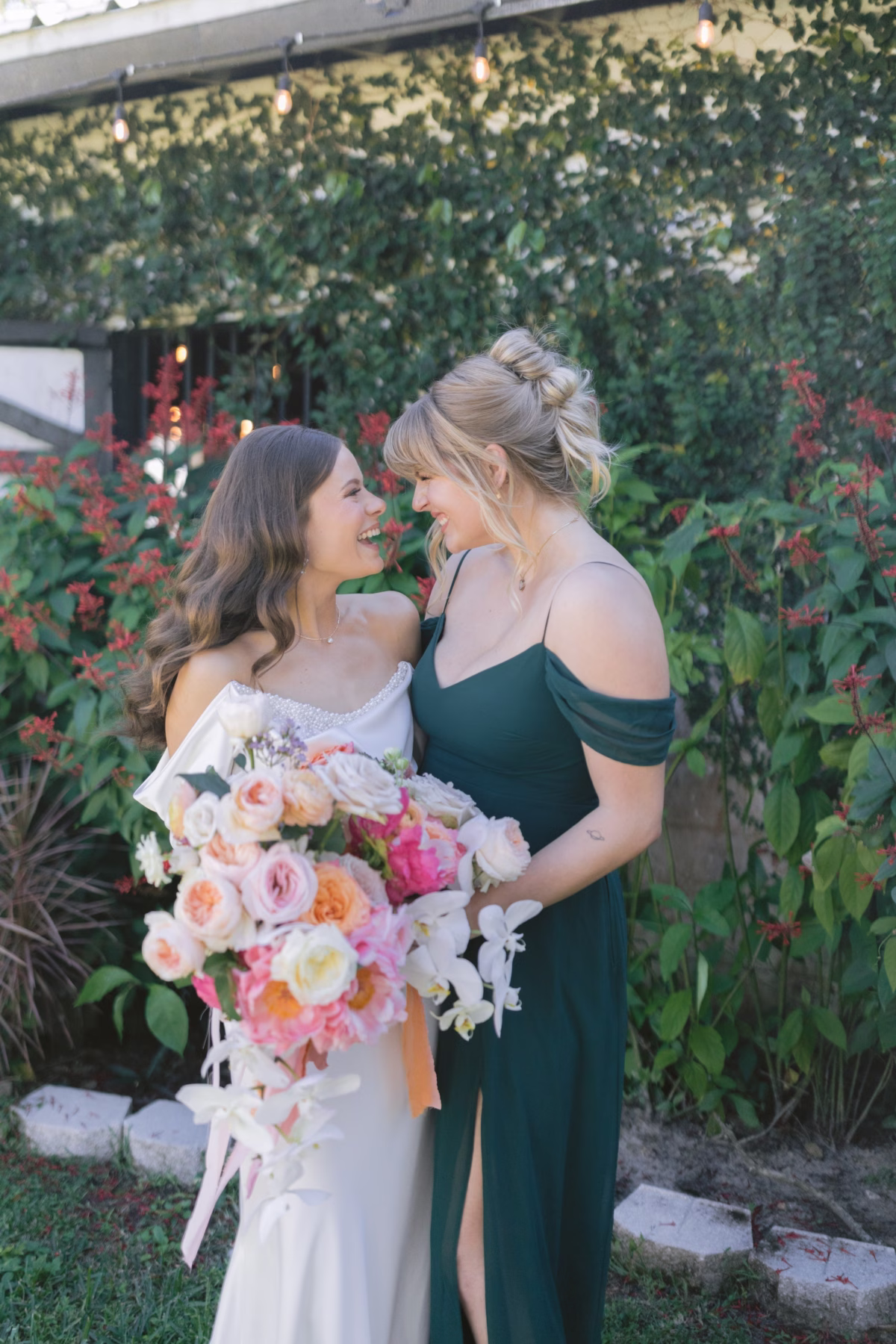 Bride in white dress and bridesmaid in emerald green dress sharing a joyful moment with colorful bouquet by Golden Wild Florals at Soire Estate Tampa garden wedding