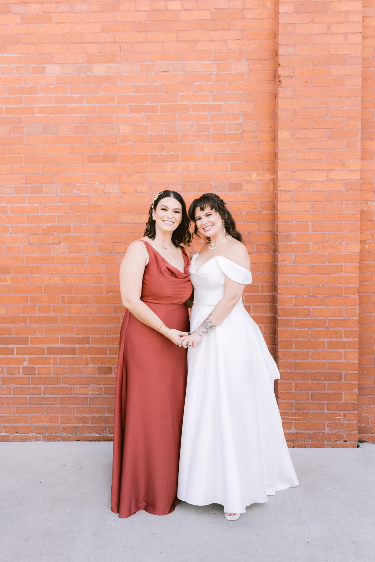 Bride in white off-shoulder gown with bridesmaid in terracotta dress at Armature Works Tampa wedding photographed by Ashley Izquierdo Photography