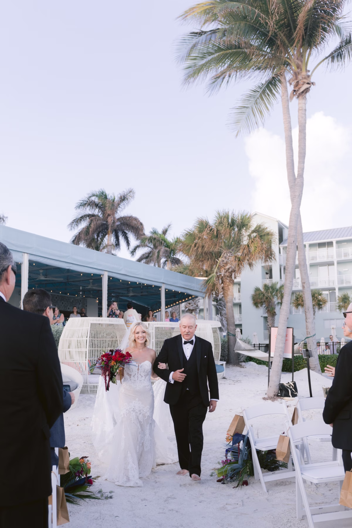 Bride in white gown walks down sandy aisle with father during beach wedding processional at Casa Marina Key West with palm trees and tropical setting