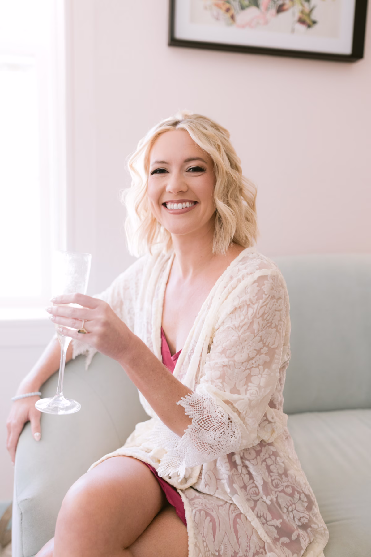 Bride in white lace robe holding champagne during getting ready at Casa Marina Key West wedding photographed by Ashley Izquierdo Photography with hair and makeup by Adore Bridal