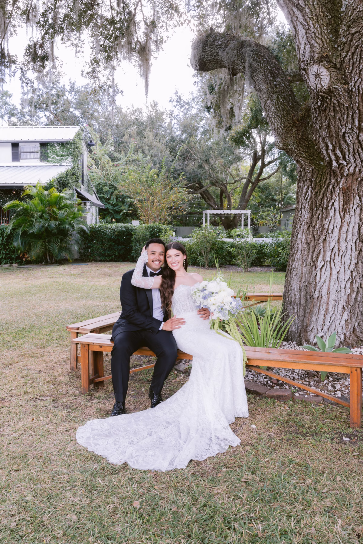 Bride and groom sitting on wooden bench in garden setting at Soire Estate Tampa wedding photographed by Ashley Izquierdo Photography