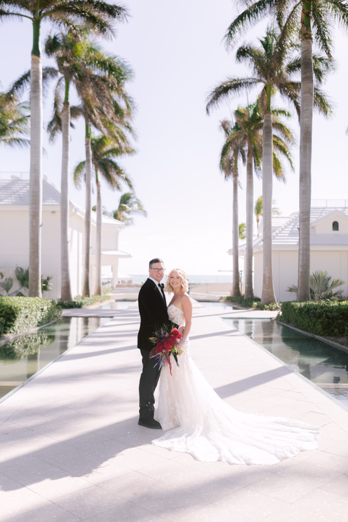 Bride and groom portrait with red bouquet by Arms of Persephone at Casa Marina Key West wedding venue with palm trees