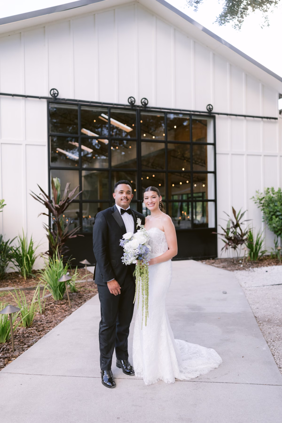 Bride in Ella Blu Bridal gown with white bouquet by Ava Elise Decor poses with groom at modern Soire Estate Tampa wedding venue