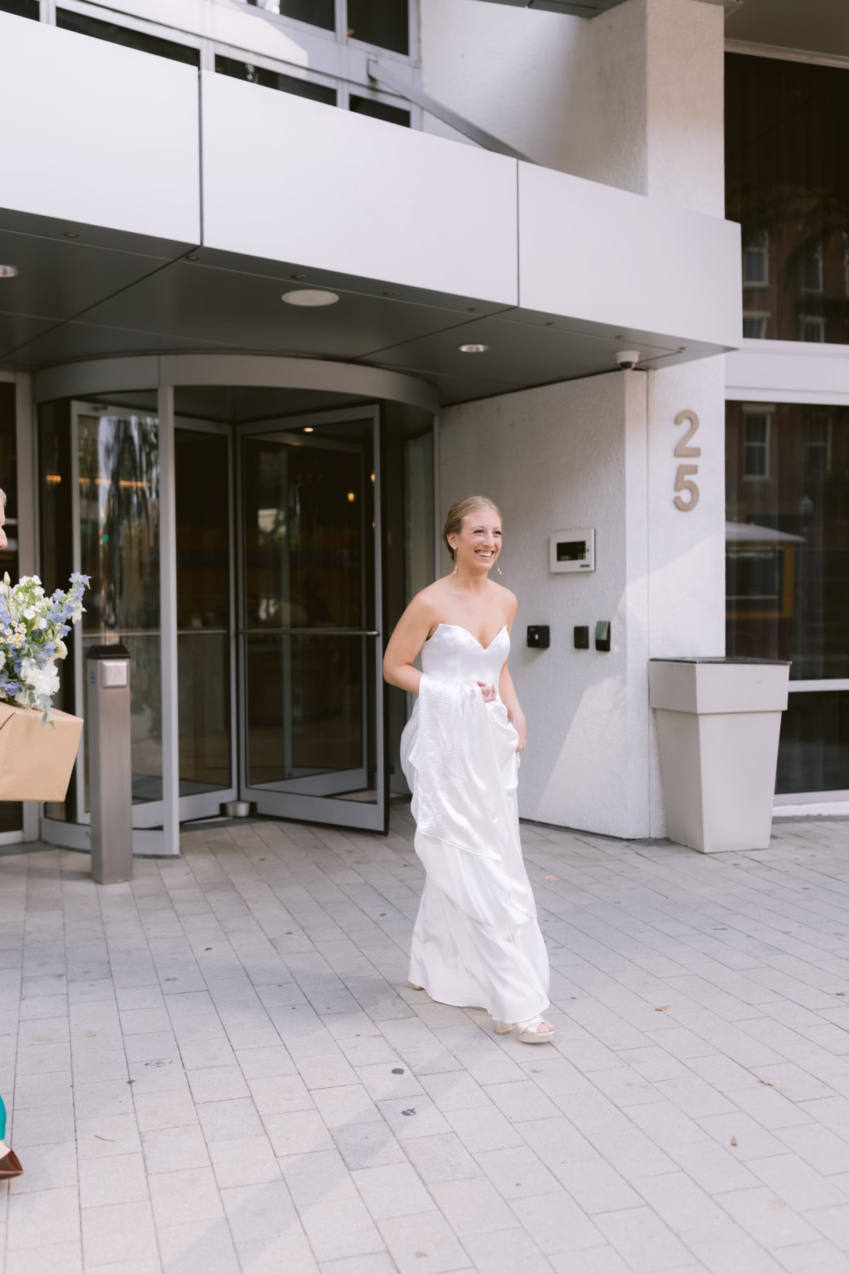 Bride in Lovely Bride DC wedding dress walking from modern building entrance in St. Petersburg captured by Ashley Izquierdo Photography
