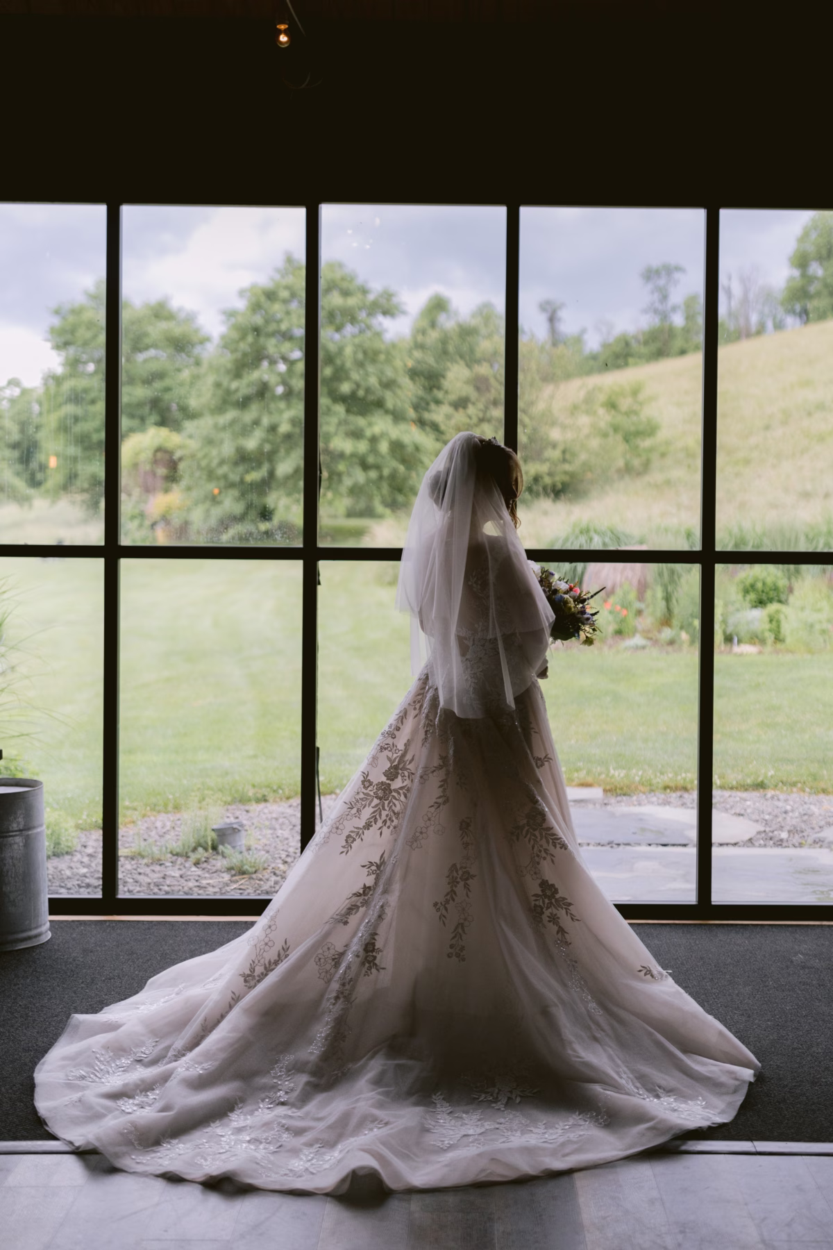 Bride in elegant Maggie Sottero wedding dress with floral embroidery and cathedral train looking out window at Red Maple Vineyard