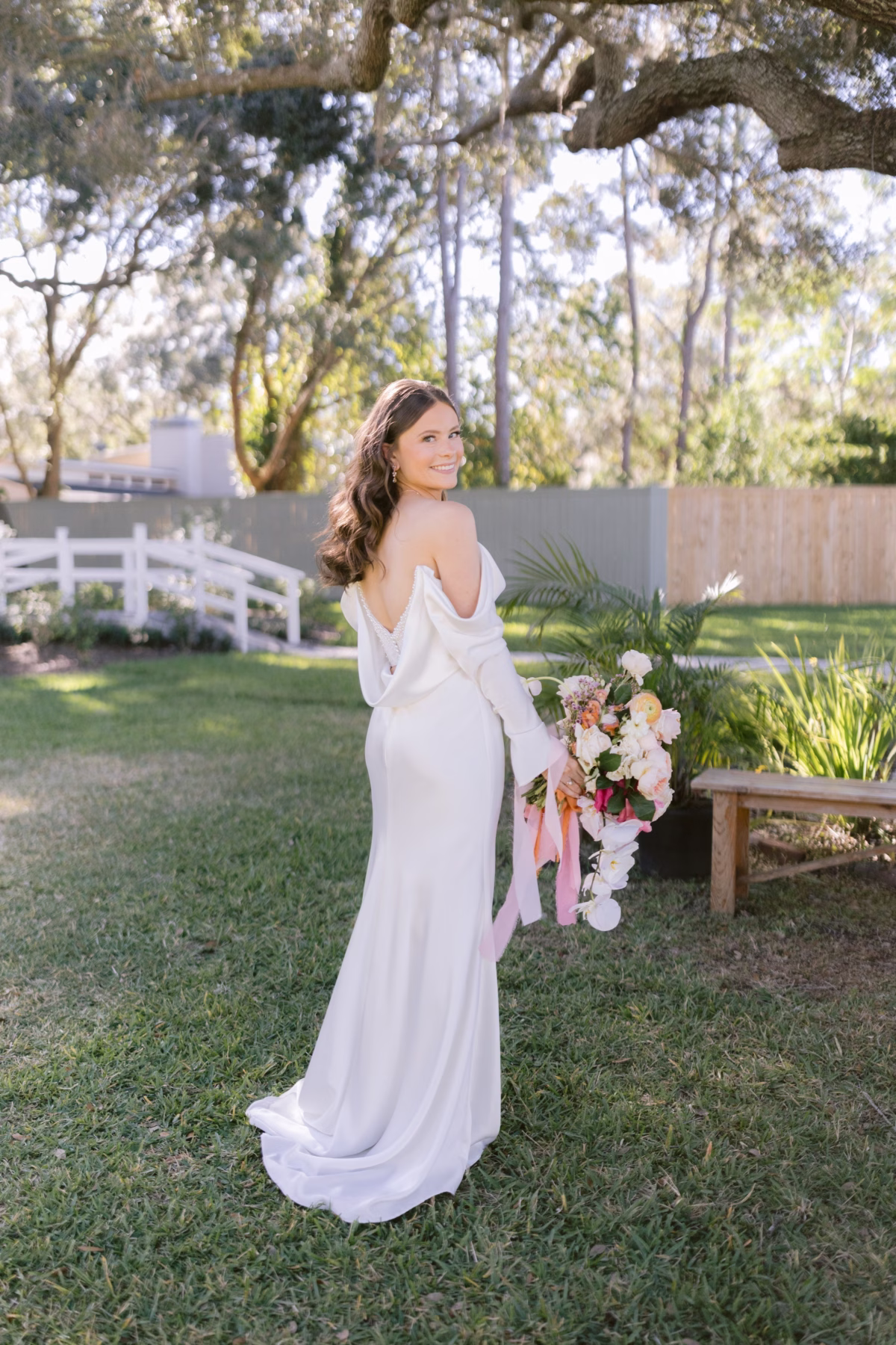 Bride in elegant white wedding dress holding colorful bouquet by Golden Wild Florals at Soire Estate garden wedding in Tampa