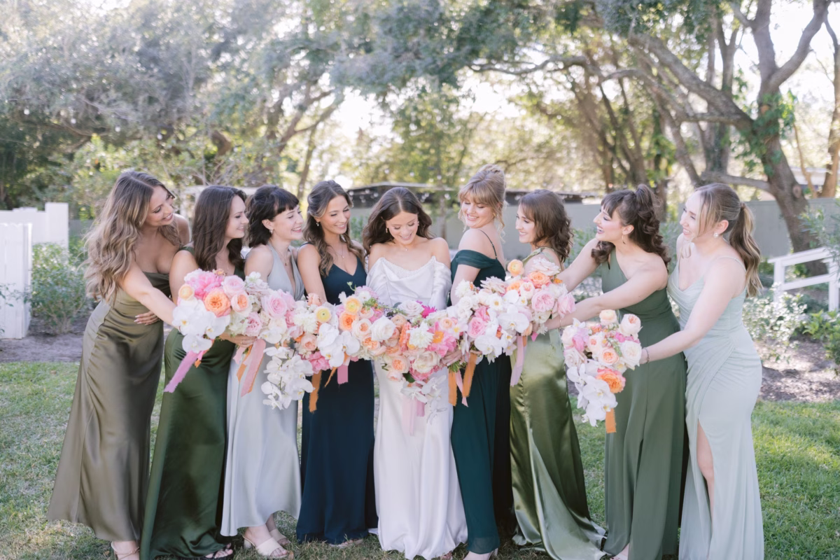 Bridesmaids in green dresses holding pink and peach bouquets by Golden Wild Florals at Soire Estate Tampa garden wedding