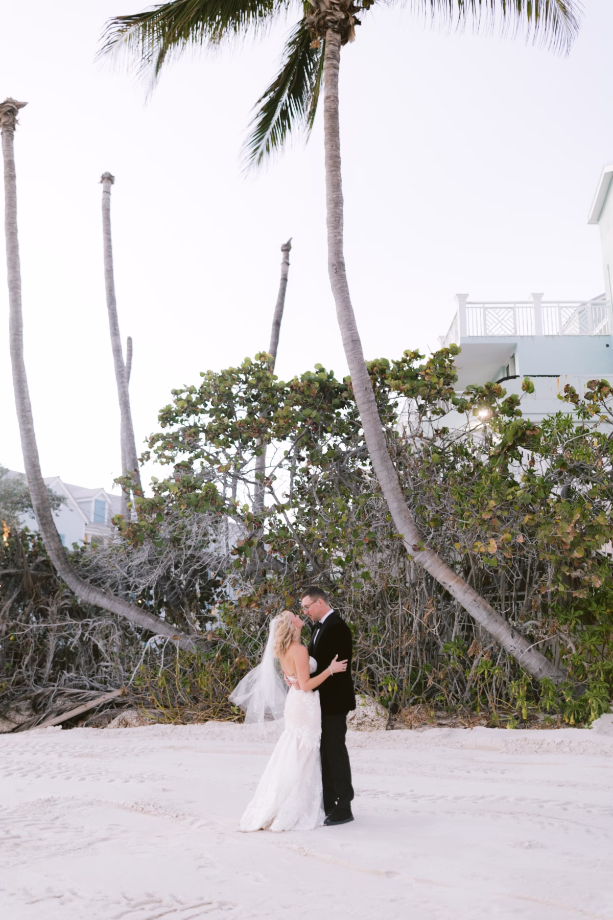 Bride and groom embrace on the beach at Casa Marina Key West with palm trees and tropical vegetation photographed by Ashley Izquierdo Photography