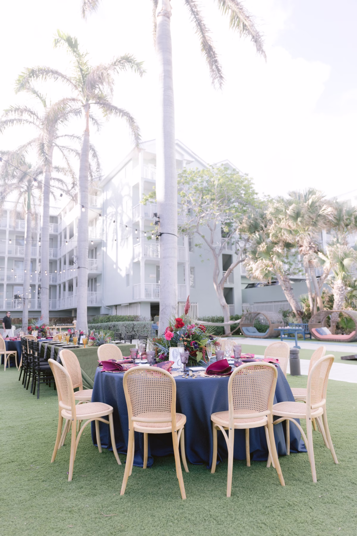 Elegant outdoor wedding reception at Casa Marina Key West with navy blue linens, natural cane chairs, and tropical florals by Arms of Persephone