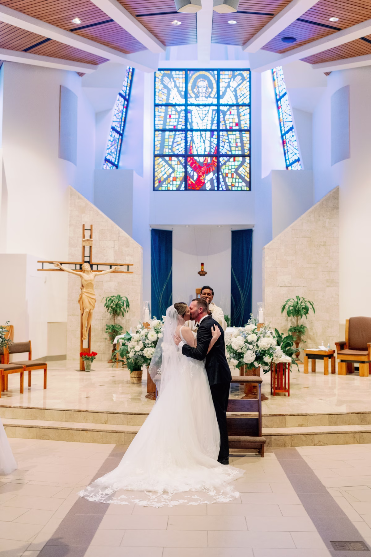 Bride and groom share their first kiss during church wedding ceremony with white floral arrangements by Lemon Drops Weddings and Events in St. Petersburg