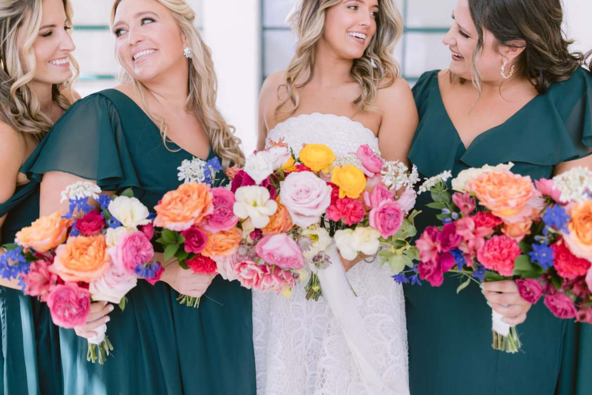 Bride and bridesmaids in emerald dresses holding vibrant colorful bouquets by Petite Fleur at St. Pete Shuffleboard Club wedding