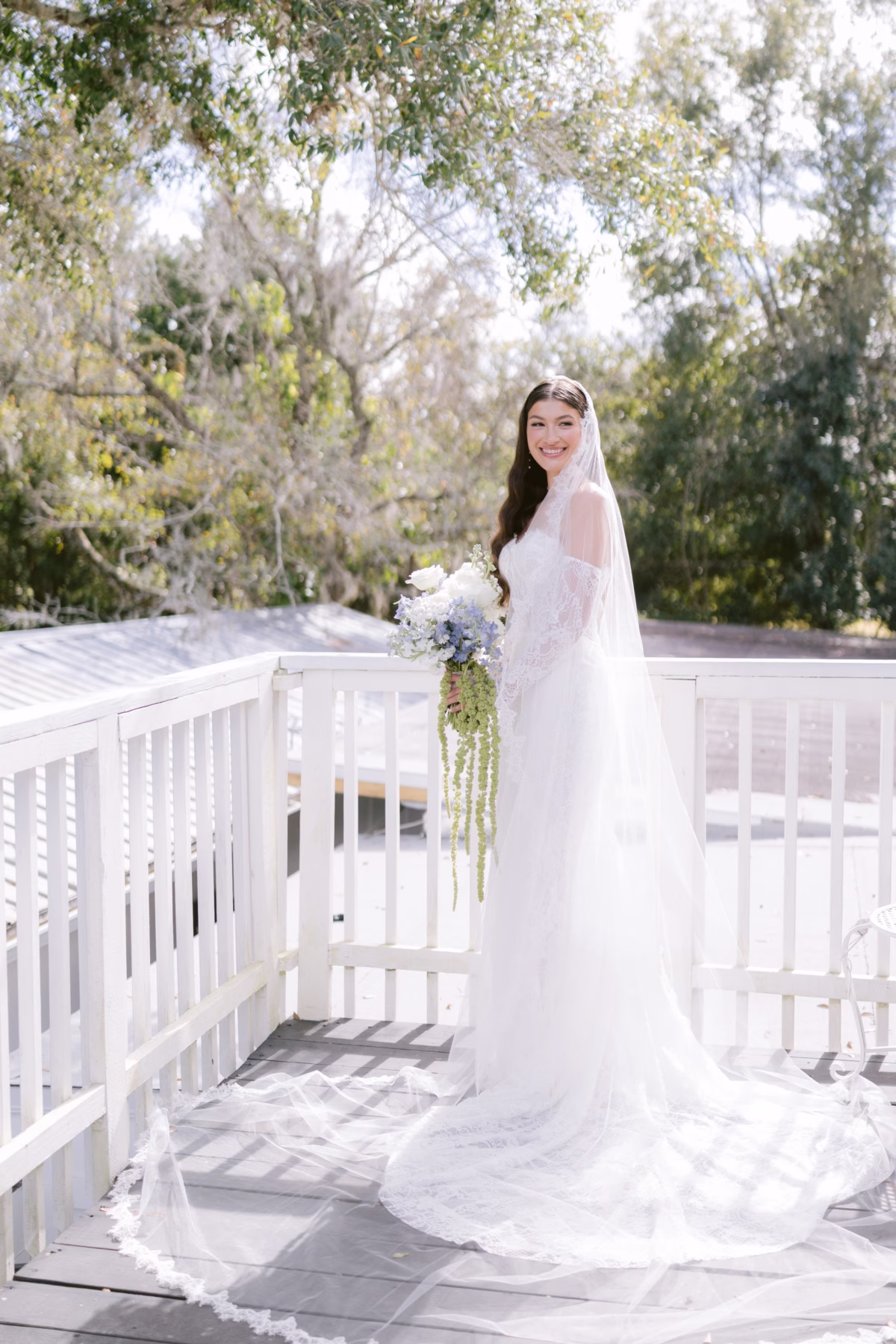 Bride in Ella Blu Bridal wedding dress holding Ava Elise Decor bridal bouquet on white wooden deck at Soire Estate Tampa wedding