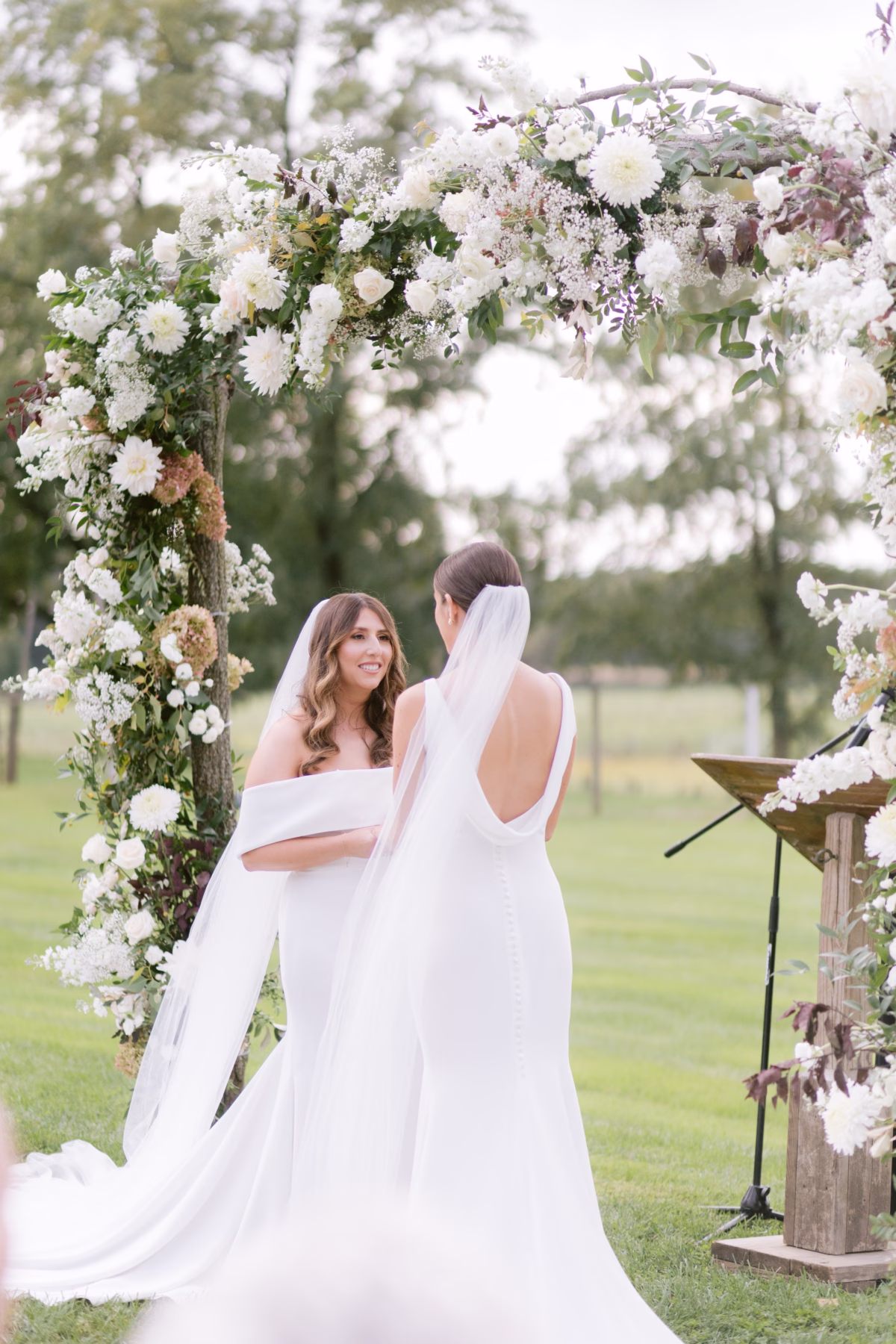 florist allie johnson white floral arch johnsons locust hall wedding - A Farm Wedding at Johnson's Locust Hall, New Jersey Two brides exchanging vows under white floral ceremony arch by Allie Johnson at Johnson's Locust Hall farm wedding in New Jersey