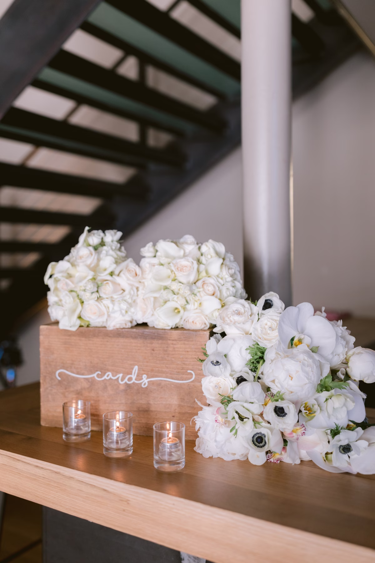 White and blush wedding flower arrangements by Maky The Diva Flowers displayed on wooden card table at The Roundhouse Beacon Hudson Valley wedding venue