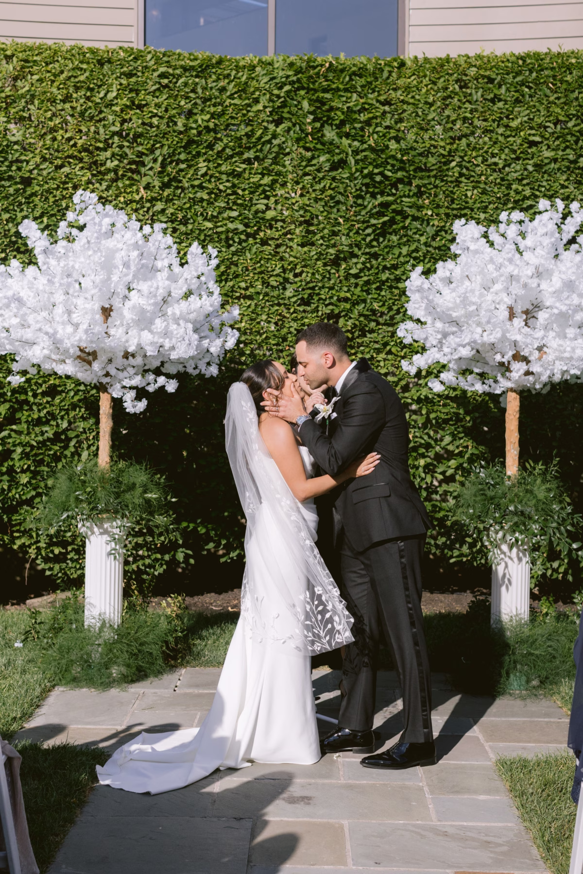 Bride and groom share first kiss at outdoor wedding ceremony with white floral arrangements by Maky The Diva Flowers at The Roundhouse Beacon