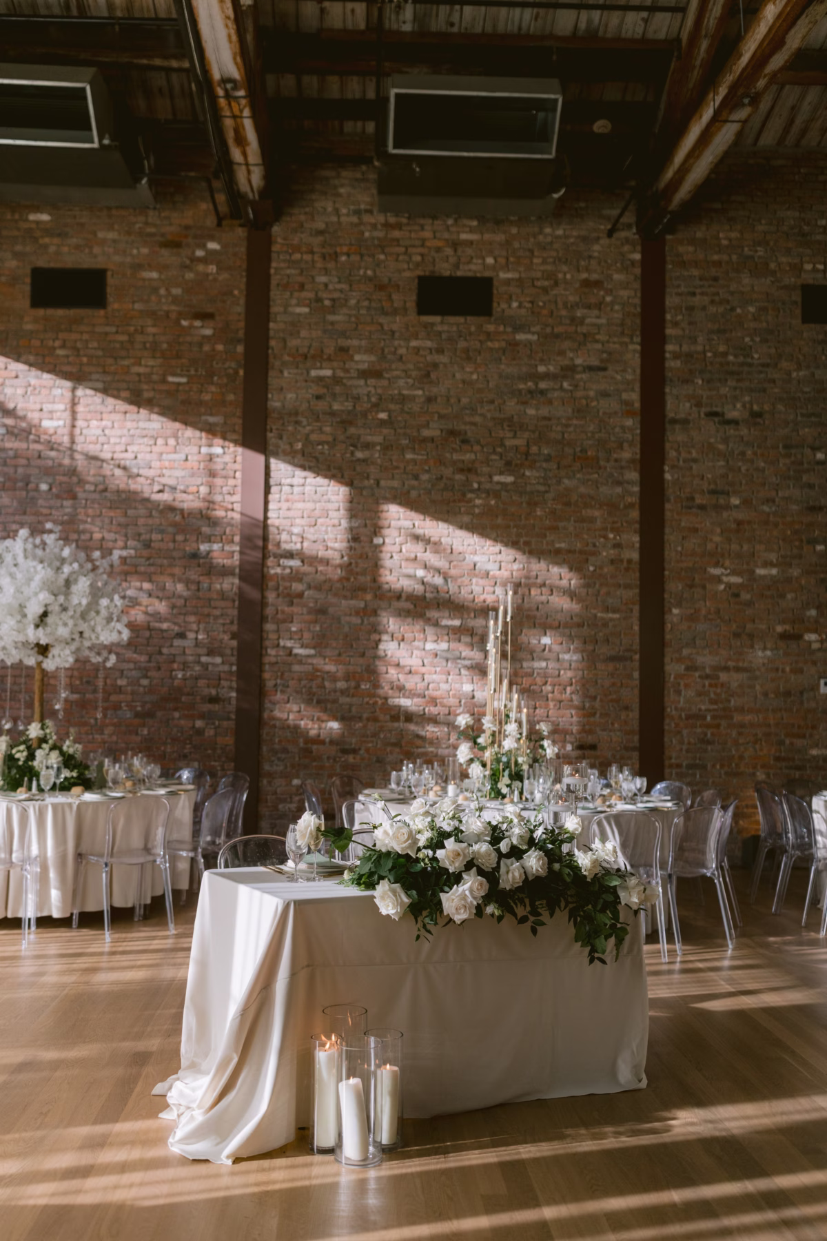 Elegant white floral centerpieces by Maky The Diva Flowers at The Roundhouse Beacon wedding reception with exposed brick walls and natural lighting