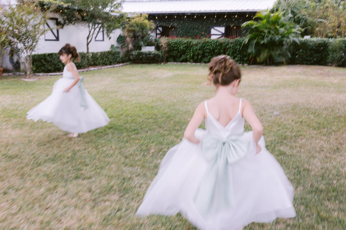Flower girls in white dresses running across lawn at Soire Estate Tampa wedding photographed by Ashley Izquierdo Photography
