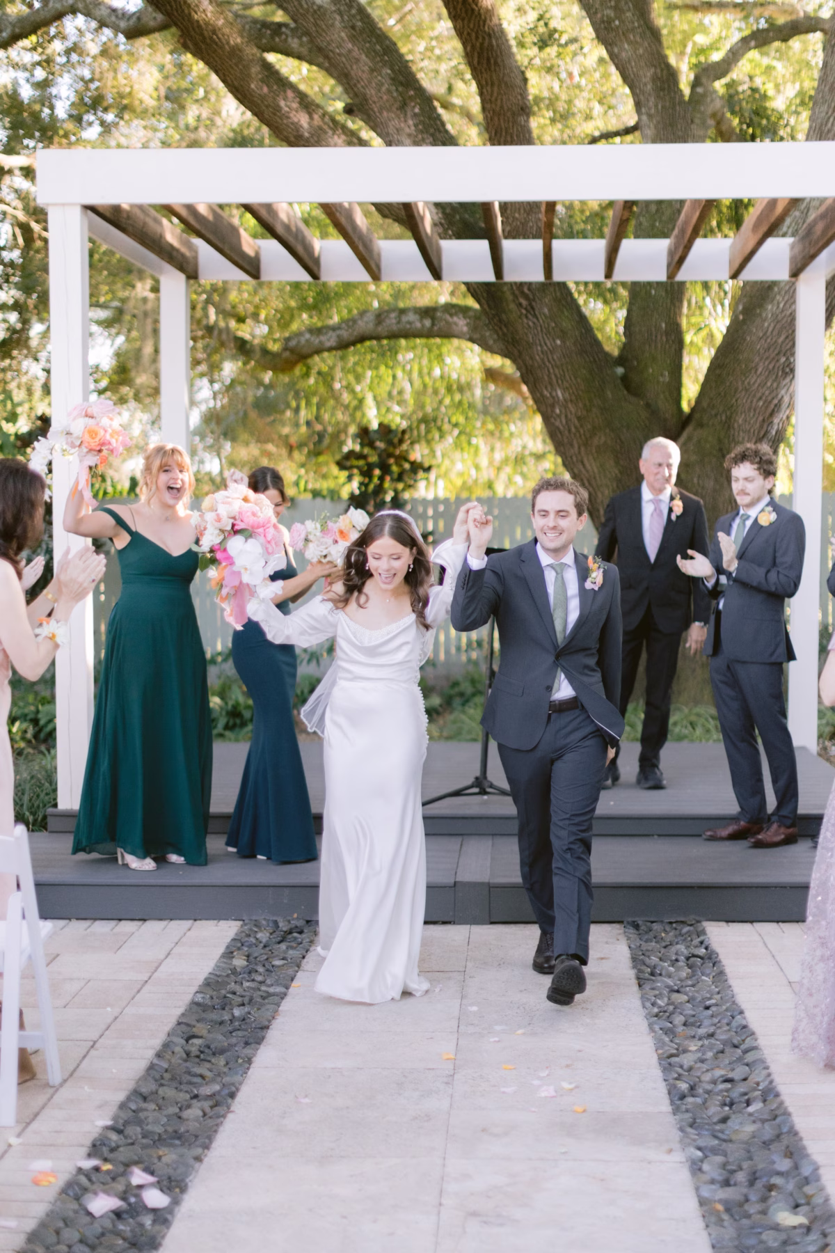 Bride and groom celebrate during wedding ceremony recessional at Soire Estate garden wedding in Tampa with bridal party cheering