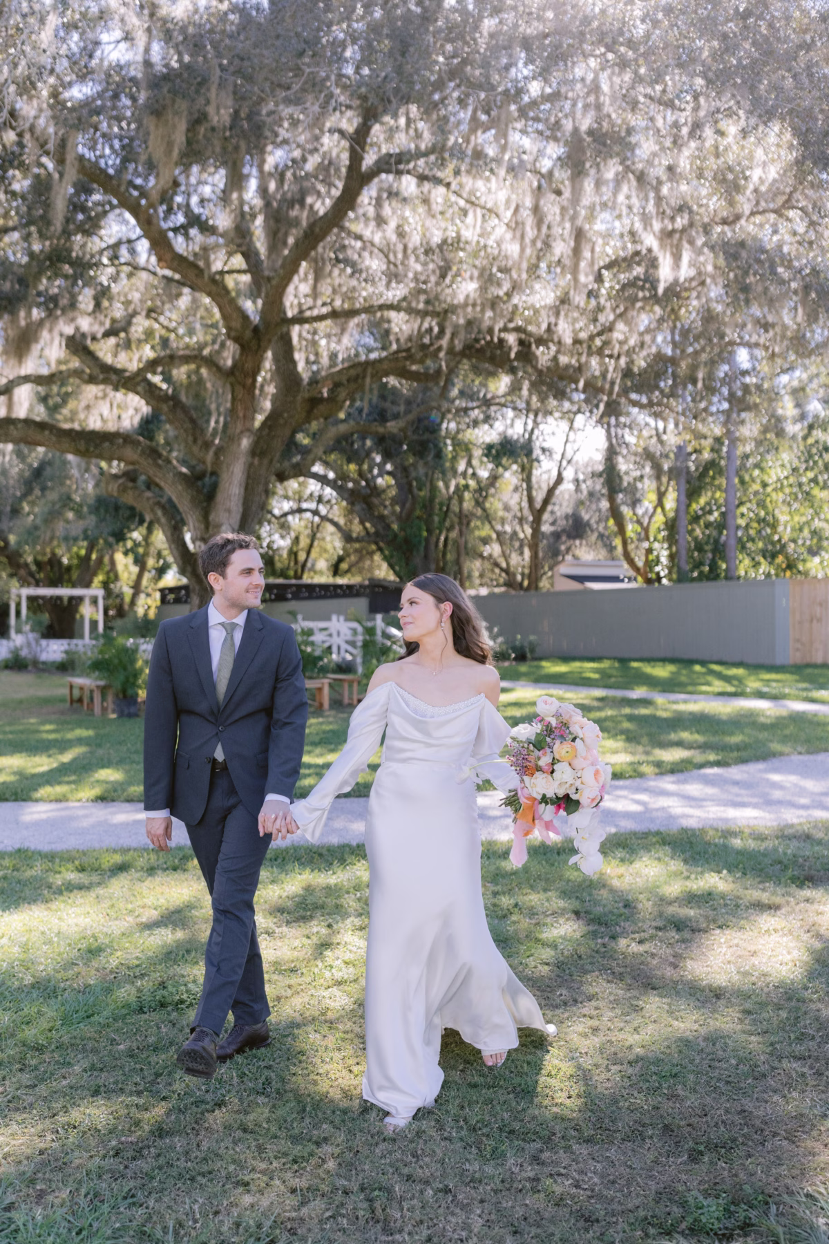 Bride and groom walking hand in hand through garden at Soire Estate Tampa wedding with Golden Wild Florals bouquet