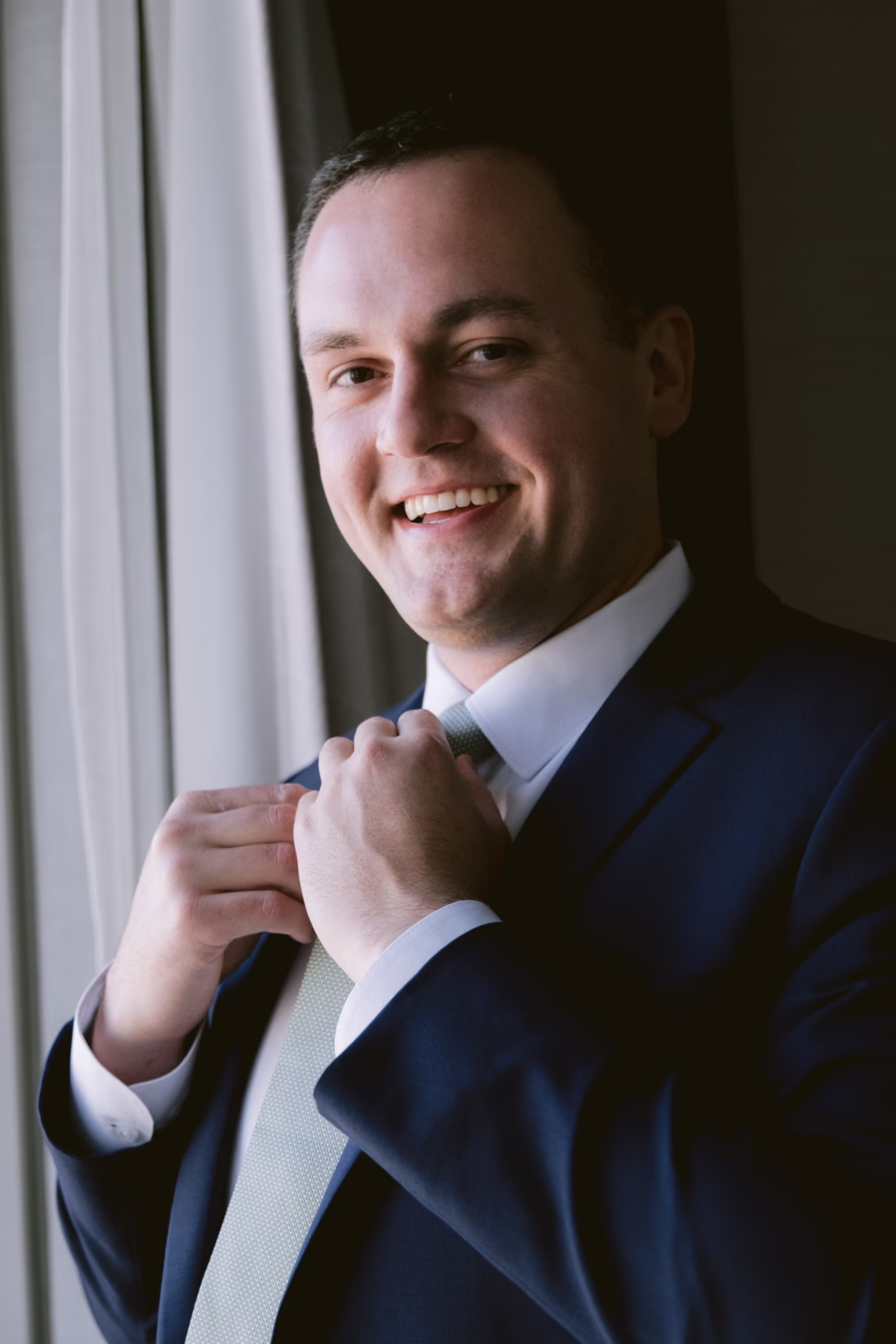Groom adjusting his tie in Men's Wearhouse suit while getting ready at JW Marriott Tampa for his Armature Works wedding