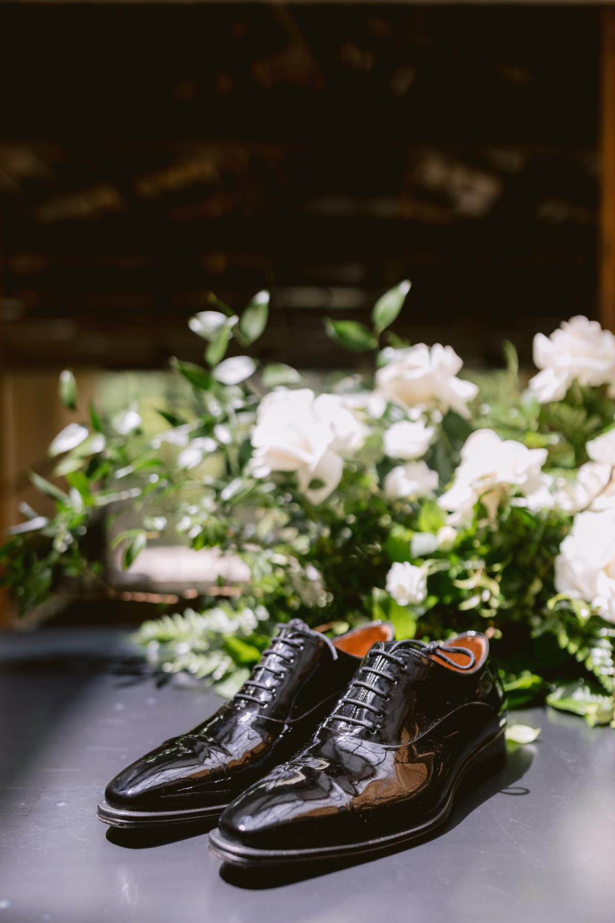 Black patent leather groom dress shoes positioned next to white bridal bouquet by Maky The Diva Flowers at The Roundhouse Beacon wedding venue