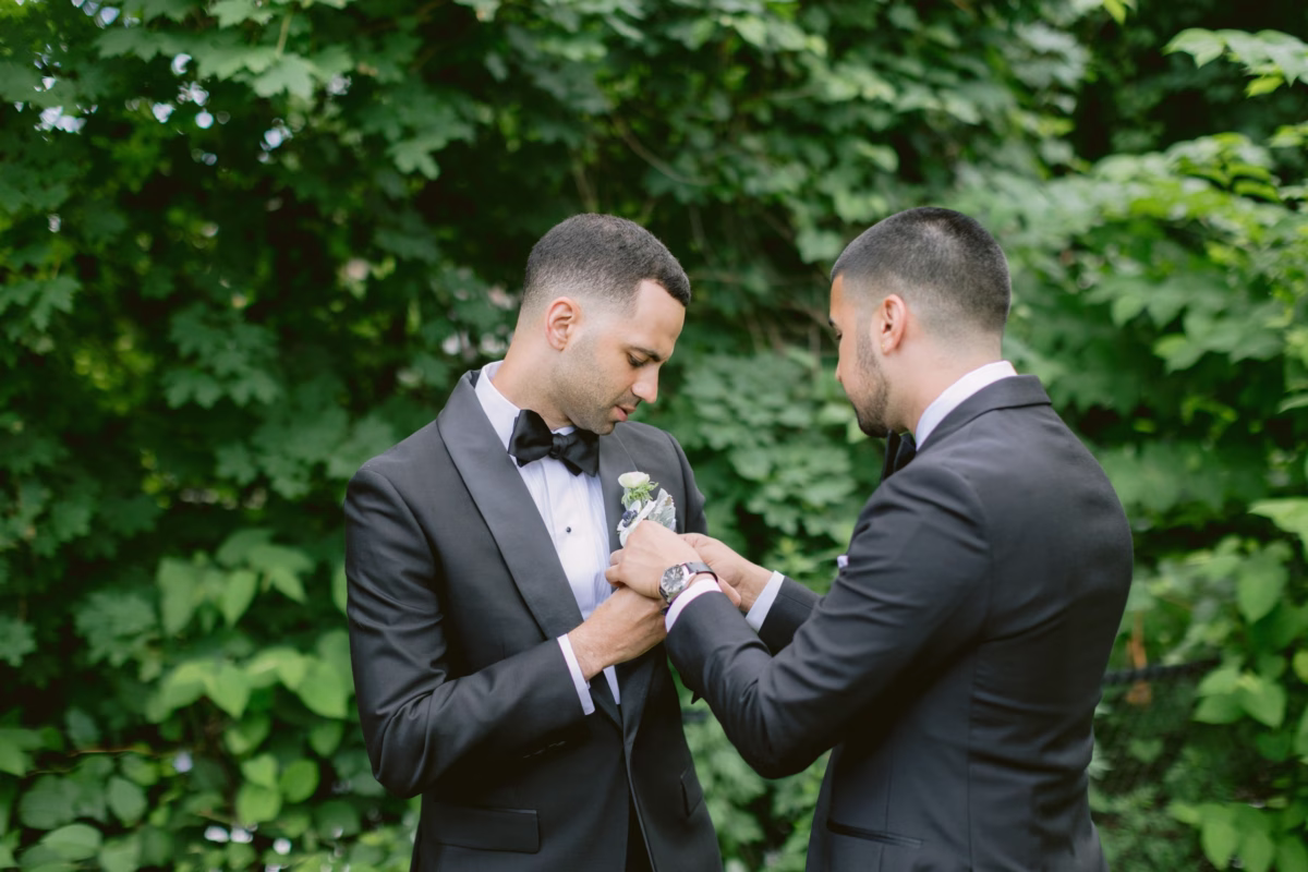 Groom getting boutonniere pinned by groomsman with white flowers by Maky The Diva Flowers at The Roundhouse Beacon Hudson Valley wedding