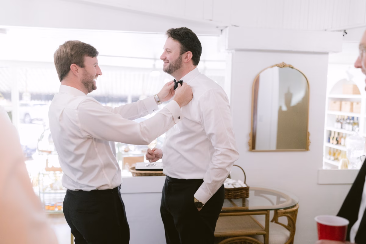 Groom getting ready with groomsmen help adjusting bow tie in formal Black Tux attire at St Pete Shuffleboard Club wedding