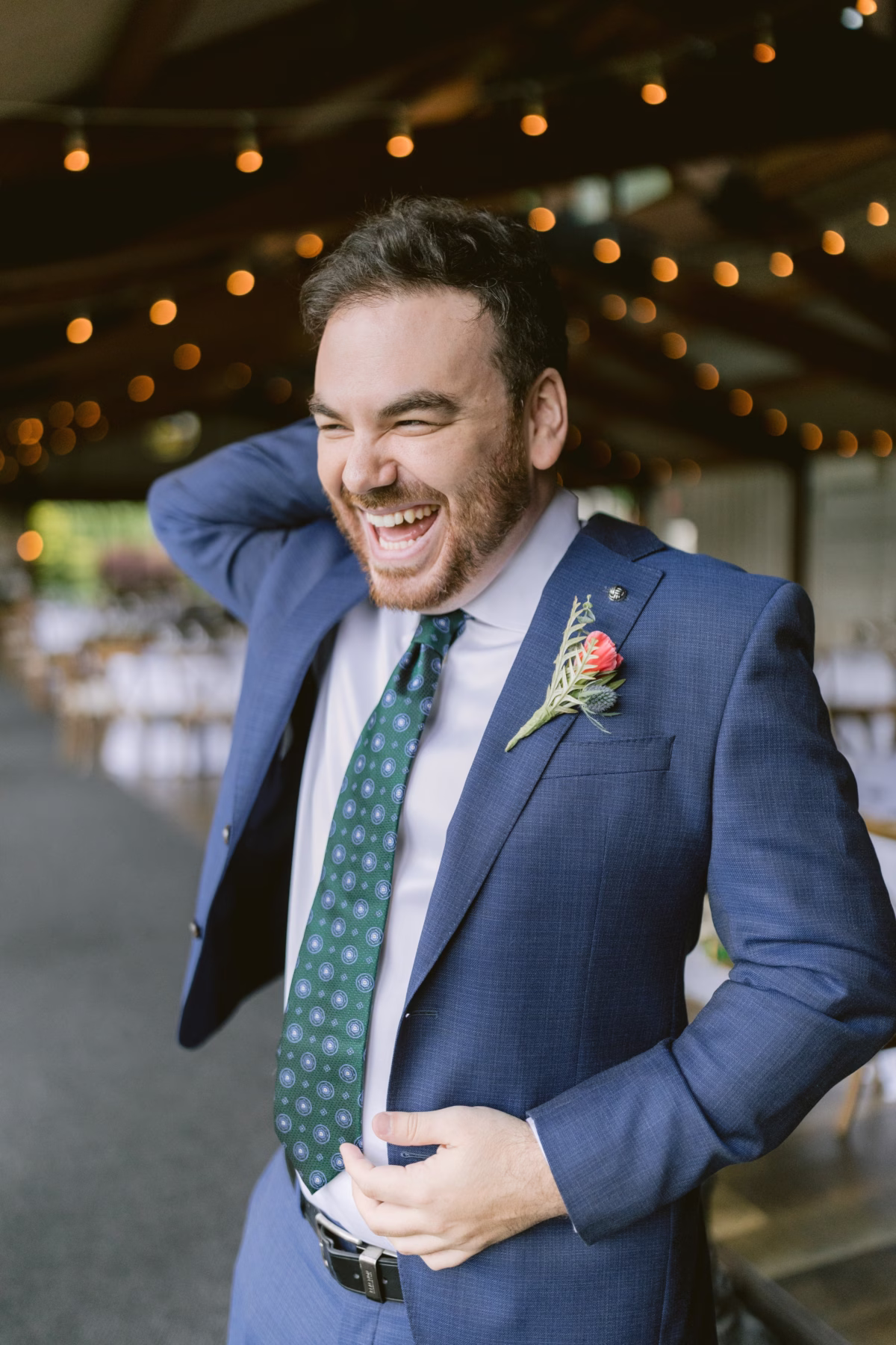Groom in navy suit laughing joyfully with Cherry Brandy Designs boutonniere at Red Maple Vineyard wedding photographed by Ashley Izquierdo Photography