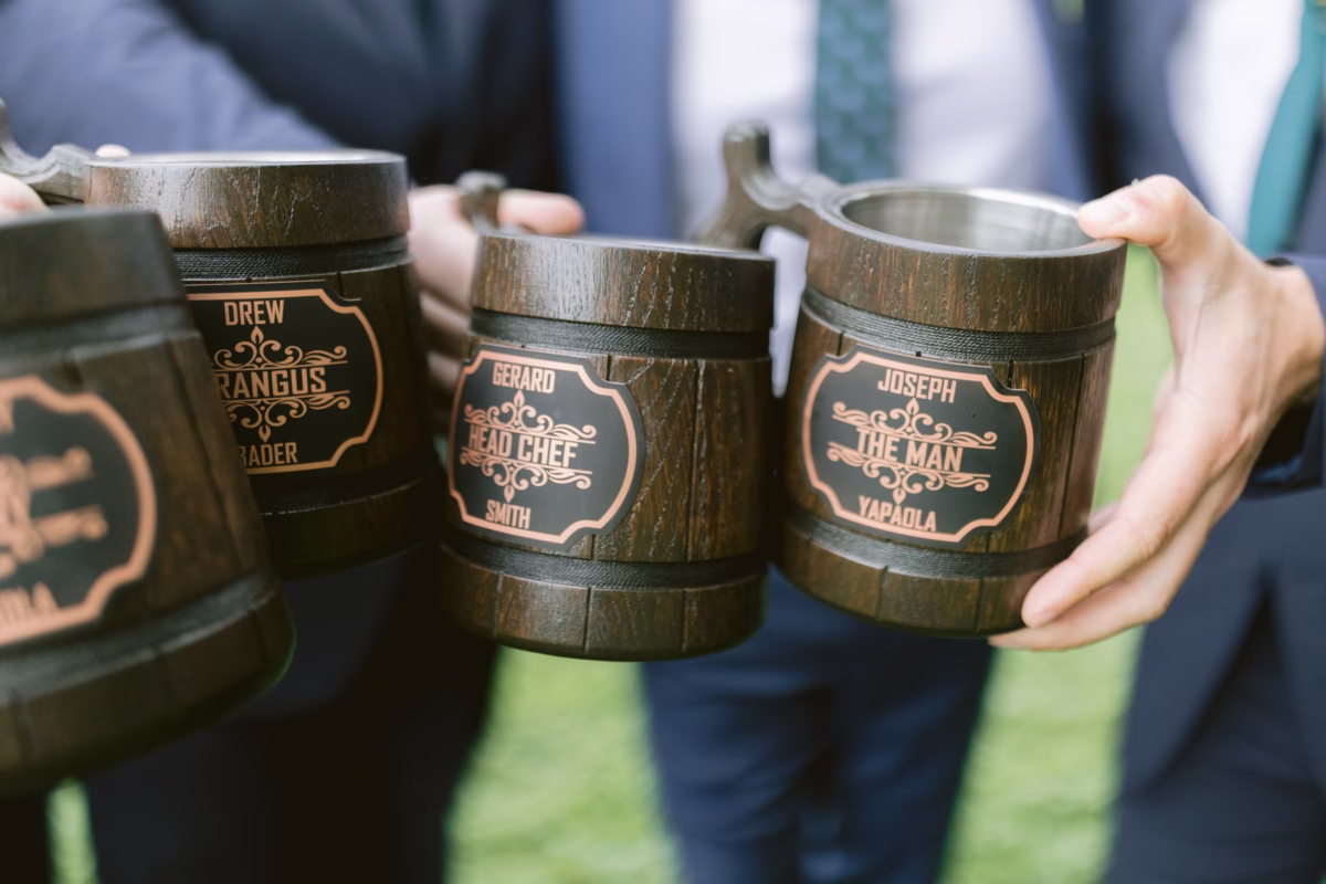 Groomsmen holding personalized wooden beer mugs with engraved names at Red Maple Vineyard wedding photographed by Ashley Izquierdo Photography