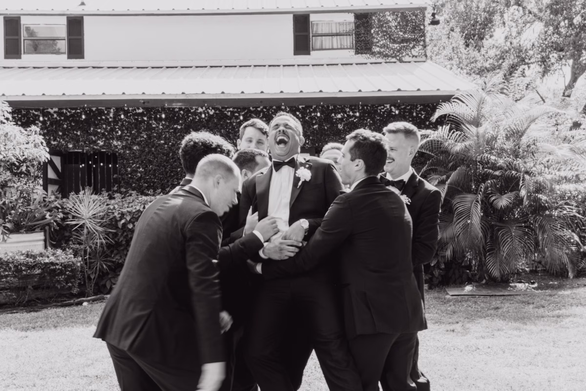 Groomsmen in black suits sharing celebratory group hug at Soire Estate Tampa wedding photographed by Ashley Izquierdo Photography