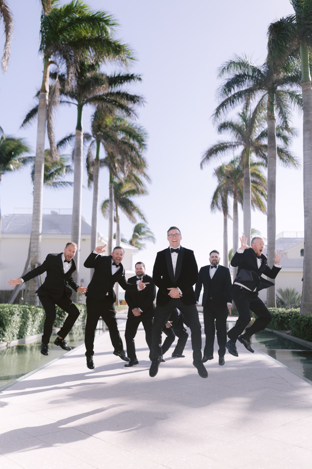 Groomsmen in black tuxedos jumping playfully during wedding celebration at Casa Marina Key West photographed by Ashley Izquierdo Photography