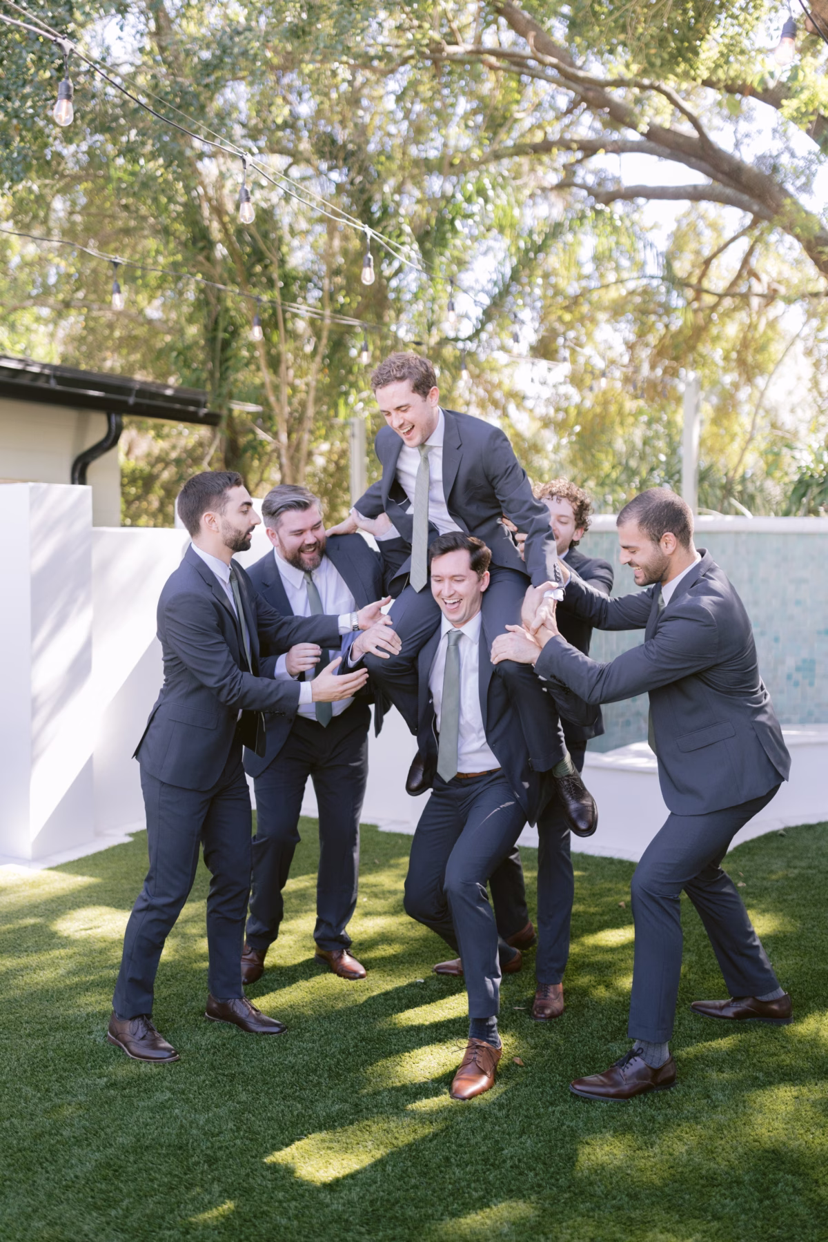 Groomsmen in gray suits lifting groom in celebratory moment at Soire Estate Tampa wedding photographed by Ashley Izquierdo Photography