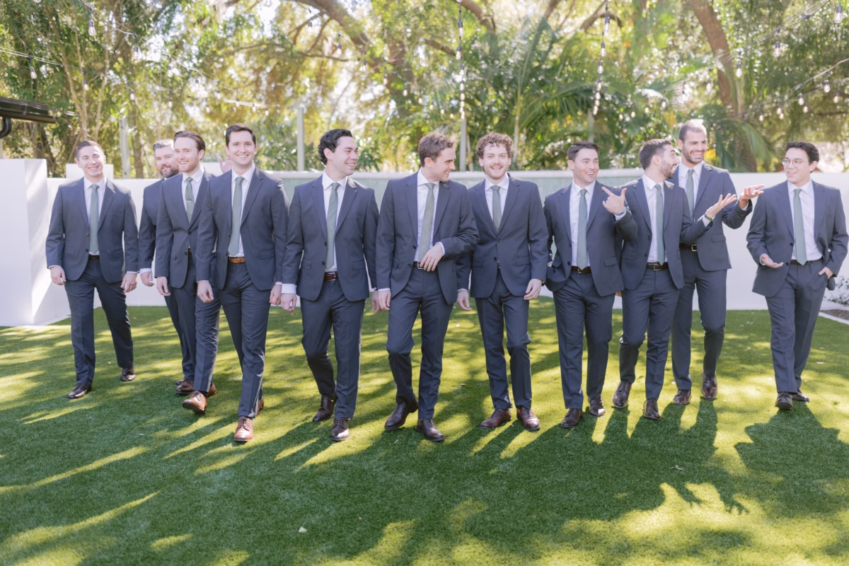 Groomsmen in navy suits walking on manicured lawn at Soire Estate garden wedding in Tampa photographed by Ashley Izquierdo Photography