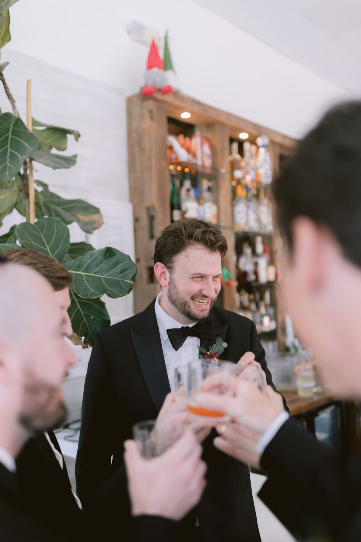Groomsmen in black tuxedos from The Black Tux raising glasses in a toast at the bar during a St. Pete Shuffleboard Club wedding