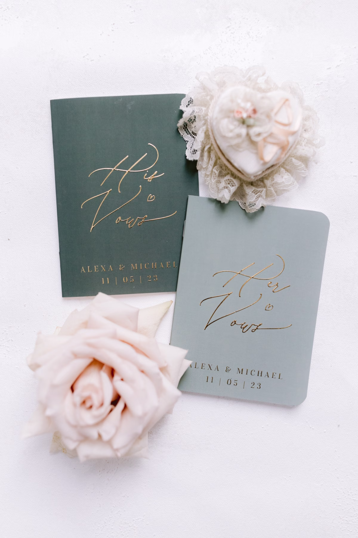 His and hers wedding vow booklets with gold calligraphy by Papier stationery surrounded by blush roses at Soire Estate Tampa wedding photographed by Ashley Izquierdo Photography