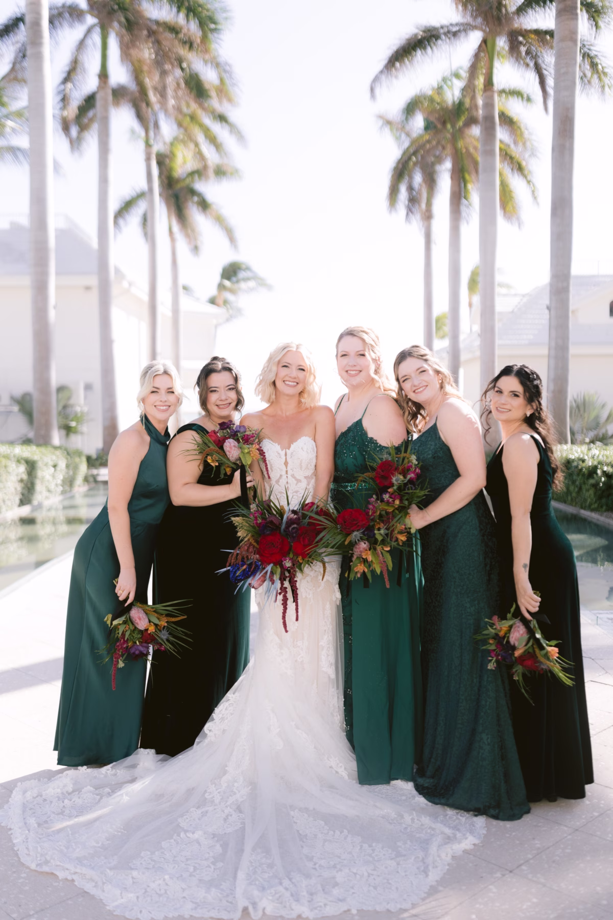 Bride in white gown with bridesmaids in emerald green dresses holding tropical bouquets by Arms of Persephone at Casa Marina Key West wedding