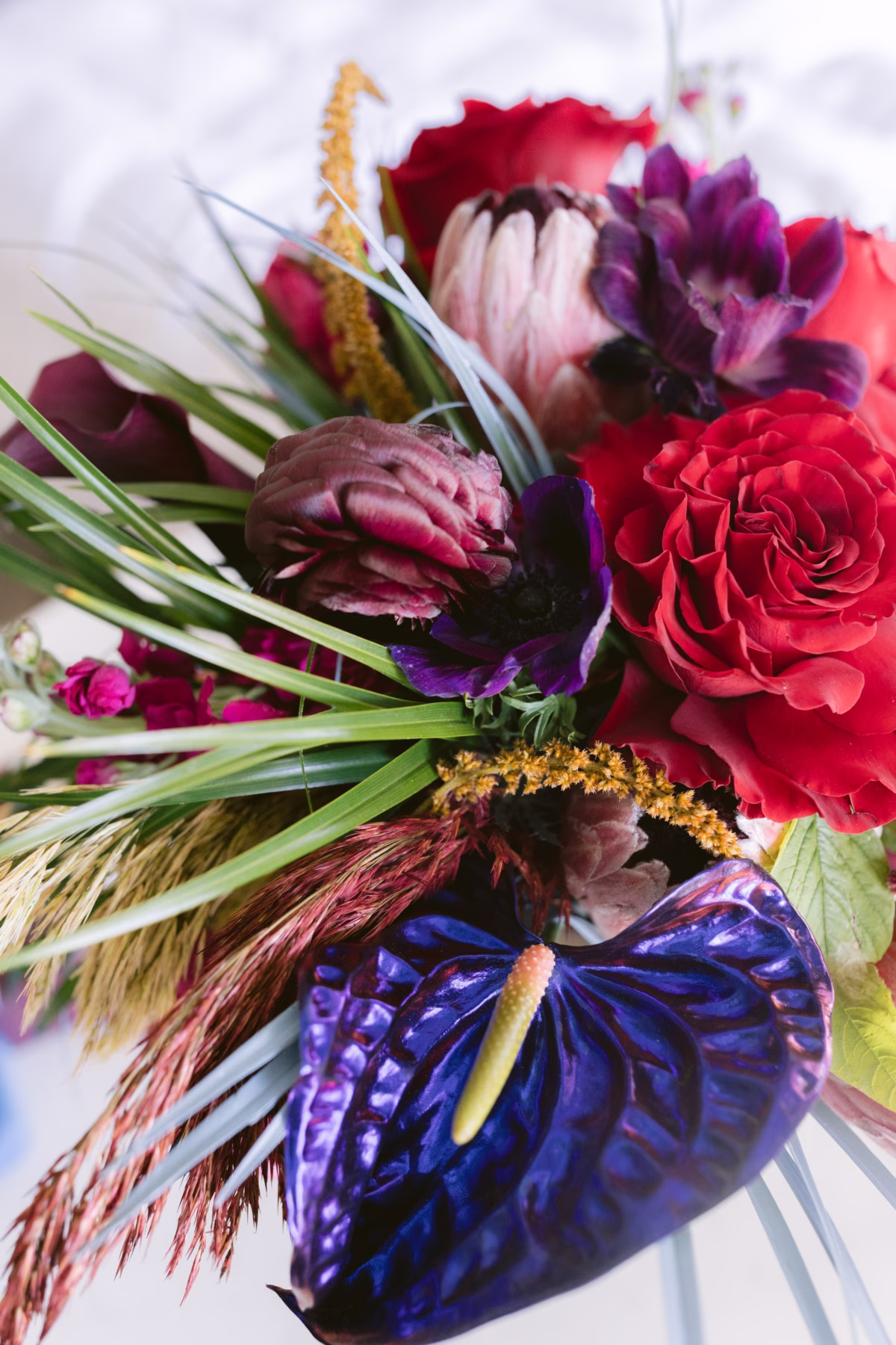 Vibrant jewel tone wedding bouquet with red roses, purple anthurium, and tropical elements by Arms of Persephone florist at Casa Marina Key West wedding photographed by Ashley Izquierdo Photography
